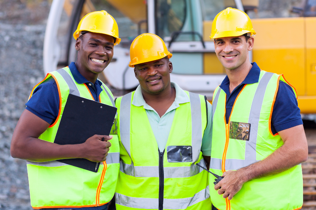 Three construction workers with yellow hard hats and bright yellow vests on a construction site.